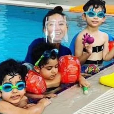 Coach Mary in the pool with three young students wearing arm floats and goggles