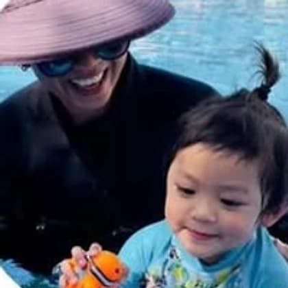 Coach Mary smiling in the water with a toddler holding a clownfish toy